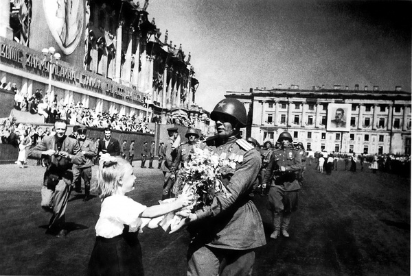 Девочка дарит цветы Герою Советского Союза гвардии полковнику Анатолию Георгиевичу Афанасьеву, идущему во главе сводной роты 63-й гвардейской стрелковой дивизии, во время парада на Дворцовой площади Ленинграда. 08.07.1945. Автор: Давид Трахтенберг