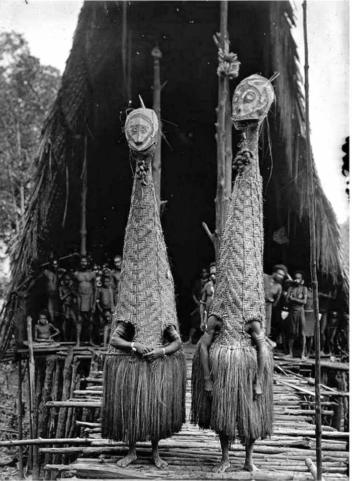 Dancers in costume in front of a men's house in the village of Towei, Papua New Guinea, 1921. - The photo, Papua New Guinea